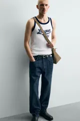 Camiseta sin mangas slim fit color blanco, con cuello redondo y sisas ribeteadas en azul marino. Estampado frontal con la palabra "League" y el número "'86" en azul marino.