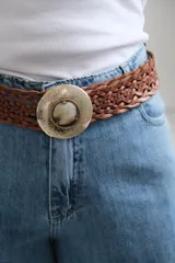 Cinto de cuero trenzado color marrón chocolate, con hebilla circular metálica grabada y detalle central de piedra natural.