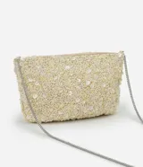 Cartera bandolera pequeña de forma rectangular, completamente cubierta de lentejuelas y cuentas brillantes en tono crema. Cuenta con cierre superior y una correa de cadena metálica plateada.