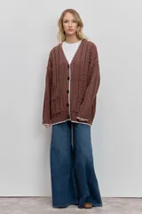 Cardigan de punto con diseño de trenzas, color marrón, con cierre frontal de botones y detalle de borde en color blanco. Presenta bolsillos frontales y mangas largas.