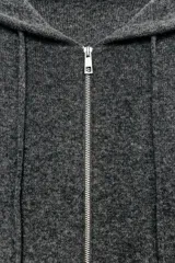 Chaqueta de punto con capucha, manga larga y cierre frontal con cremallera metálica. Presenta un diseño de tejido texturizado en color gris oscuro con detalles en contraste en los puños.