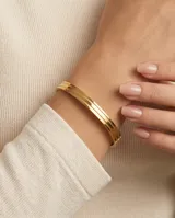 Pulsera tipo esclava rígida de acero con baño de oro, con diseño de líneas paralelas y acabado pulido.
