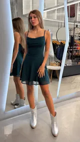 Vestido corto de fiesta color verde oscuro con acabado brillante y sutiles destellos. Presenta escote tipo cowl (caído), breteles finos y falda evasé con caída fluida.