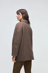 Chaquetón de lana fina sin teñir, con cuello camisero, cierre frontal de botones y bolsillos delanteros. Diseño de corte recto y estructura clásica.