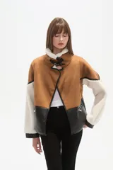 Chaqueta estilo aviador o biker, con paneles de color marrón (simil gamuza), negro (simil cuero acolchado) y blanco (simil borrego/sherpa). Presenta cuello solapa ancho forrado en blanco, detalles de hebillas negras en los hombros y cierres metálicos en la parte delantera.