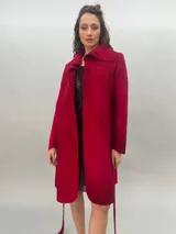 Tapado rojo de lana merino afieltrada, corte recto con lazos para ajustar en la cintura y cuello alto con posibilidad de cruzar los lazos alrededor. Tiene bolsillos laterales.