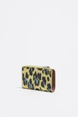 Billetera mediana con exterior rígido y textura brillante, con estampado de leopardo en tonos azul celeste, negro y naranja. Presenta cierre de cremallera y logo metálico de Bimba y Lola en el frente.