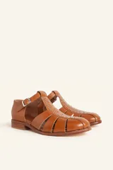 Sandalias de cuero color marrón, tipo romanas, con talón cerrado, tira en T con detalles de tachas metálicas, aberturas laterales y cierre de hebilla ajustable. Tienen tacón bajo de madera.