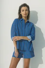 Camisa de corte relajado con diseño de rayas verticales en tonos rojos, marrones y blancos. Presenta cuello clásico, cierre frontal con botones al tono y mangas largas con puños que permiten un estilo arremangado.