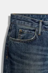 Jeans de tiro medio con corte baggy y diseño de cinco bolsillos. Presenta un efecto lavado, cierre frontal con cremallera y botón, y bajo con acabado en vuelta.