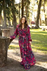 Vestido largo de lino con escote cruzado, mangas largas abullonadas y lazo ajustable en la cintura. Presenta un estampado floral vibrante en tonos fucsia, violeta y verde.