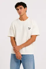 Remera de algodón color off-white, de manga corta, con cuello redondo y pequeño estampado de tres estrellas negras en el pecho.