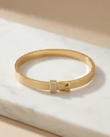 Esclava rígida de acero con baño de oro, con textura grabada y detalle de hebilla decorativa con incrustaciones de circonias.