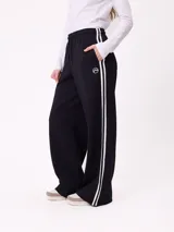 Pantalon de jogging de corte ancho, color negro con rayas laterales blancas. Posee cintura elastizada con cordón de ajuste y logo bordado en la parte frontal.