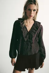 Camisa de manga larga con estampado de cuadros, escote en pico con volantes decorativos y cierre frontal con botones. Presenta puños elásticos.