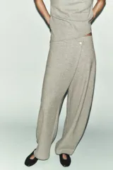 Pantalón de tiro alto con diseño cruzado frontal y cierre de botón. Presenta pierna ancha y cintura elástica, confeccionado en tejido de algodón.