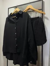Conjunto de dos piezas compuesto por una camisa de manga larga con botones frontales y un short con cintura elástica, ambos confeccionados en tela de textura arrugada color negro.