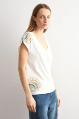 Remera blanca de manga corta, con escote en V y detalles de estampa paisley en los hombros y en el borde inferior.