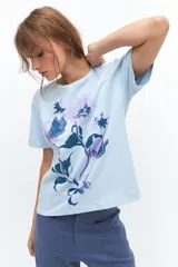 Remera lila de algodón con estampado de flores en tonos naranja y rosa.