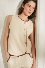 Top sin mangas de lino color beige, con cuello redondo y cierre frontal de botones con ribetes en contraste marrón oscuro.