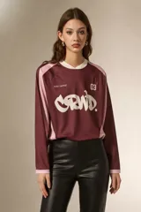 Remera de manga larga estilo deportivo, confeccionada en tejido técnico. Presenta un diseño color block en tonos bordó y rosa, con cuello mao y estampado gráfico frontal en color blanco.