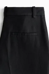 Pantalón sastrero negro de tiro alto y piernas rectas, confeccionado en mezcla de lino y lyocell. Presenta pretina con presillas, cierre con botón y corchetes ocultos, bolsillos al bies y pliegues marcados al frente y en la espalda.