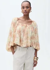 Blusa de gasa color crema con estampado de flores en tonos naranja y verde, escote cuadrado con detalle fruncido, mangas largas abullonadas y espalda abierta.