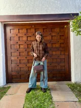 Cartera bandolera de cuero color chocolate con solapa frontal, costuras a la vista y herrajes metálicos. Incluye dos correas desmontables, una corta y una larga, y cuenta con bolsillo interior.