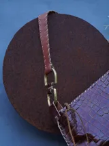 Cartera de cuero crocco con herrajes en bronce, silueta curva, terminación artesanal en los bordes y correa de hombro ajustable con detalles metálicos.