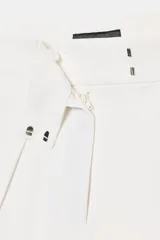 Pantalón negro de tiro medio, pierna ancha y pliegues marcados en el delantero. Presenta bolsillos laterales ocultos y cierre frontal con cremallera, botón y ganchos metálicos.