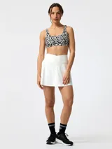 Falda short deportiva blanca, de talle alto con cintura cruzada en forma de V. Cuenta con aberturas laterales y short interior con bolsillo.