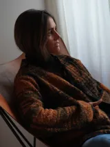 Saco abrigado de tejido texturizado en tonos marrones y negros, con diseño a cuadros, ribetes de lino en los bordes y cierre frontal con lazos.