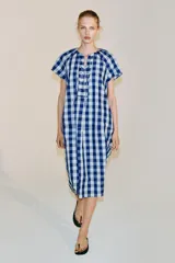 Vestido midi de Zara Woman Collection confeccionado en mezcla de viscosa, con estampado de cuadros en tonos azul y celeste. Presenta cuello redondo, manga corta, bolsillos ocultos en las costuras y cierre frontal con cordones entrelazados.