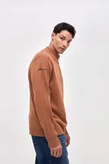 Buzo de punto color azul, con cuello alto y cierre frontal parcial. Presenta un diseño con textura acanalada en los hombros y mangas, y un pequeño bordado en la manga derecha.