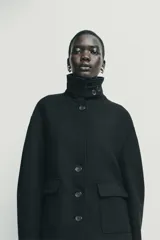 Abrigo corto de paño con mezcla de lana, color negro. Presenta cuello subido con cierre de botones, manga larga y dos bolsillos de plastrón con solapa en el frente. Cierre frontal con botones.