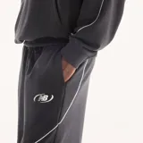 Pantalón de jogging New Balance Trackside negro de corte recto y holgado, con cintura elástica con cordón ajustable, bolsillos laterales y líneas de ribete blancas en contraste. Cuenta con un pequeño logo bordado en la pierna.