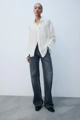 Camisa oversize blanca de cuello solapa y manga larga con puños anchos. Cuenta con cierre frontal de botones y un bolsillo aplicado en el frente.