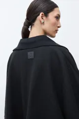 Capa negra con solapa y cuello tejido, de corte amplio y sin mangas.