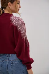 Sweater de punto color bordó, de corte cropped y mangas largas con puños ajustados. Presenta detalles decorativos de apliques bordados con lentejuelas y perlas en la zona de los hombros.