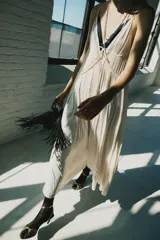 Vestido midi de satén color crudo, con escote en V, tirantes finos y detalle de lazada en el delantero.