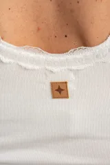 Musculosa off white de algodón peinado elastizado, con calce al cuerpo, escote redondo y detalles de encaje en el escote y los tirantes.