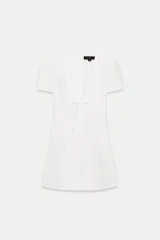 Vestido corto de Zara, color blanco, con escote en pico, mangas cortas abullonadas y detalle de lazo frontal en el mismo tejido. Presenta un corte entallado y cierre de cremallera oculta en la espalda.