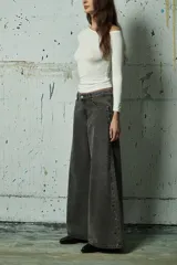 Jean de corte wide leg en color gris lavado, con diseño de aberturas laterales decoradas con tachas metálicas a lo largo de toda la pierna.