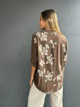 Blusa de corte holgado color chocolate con estampado floral en tonos claros. Presenta cuello camisero con tapeta frontal decorada con lentejuelas y un bolsillo en el pecho también con aplique de lentejuelas. Posee mangas tres cuartos con detalle de trabilla para arremangar.