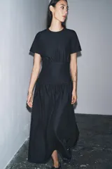 Vestido midi de denim color negro con cuello redondo y manga corta. Presenta un diseño con cintura entallada tipo bustier y falda con corte evasé. Cierre posterior con cremallera.