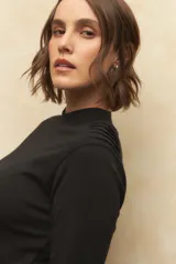 Polera de manga larga en color negro, confeccionada en algodón, con cuello alto y detalle de frunces en los hombros.