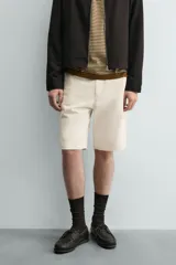Bermuda de algodón color beige claro, de corte relajado y largo hasta la rodilla. Presenta cierre frontal con cremallera y botón, bolsillos delanteros y bolsillo cerillero, además de bolsillos traseros de plastrón.