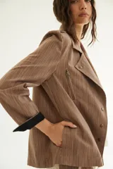 Chaqueta corta de inspiración motoquera color beige, confeccionada en lino fantasía, sin forro, con cierres decorativos, broches de presión y bolsillos delanteros funcionales. Presenta detalle bajo el cuello y en vueltas de mangas en color mostaza y rayas.