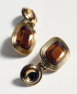 Aros colgantes dorados con diseño articulado, compuestos por una pieza circular superior con piedra semiesférica y una pieza rectangular inferior con piedra facetada color ámbar.