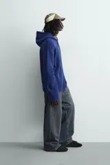 Chaqueta de punto de corte relajado, color azul, con capucha, cierre frontal con cremallera y acabados en rib en puños y bajo.